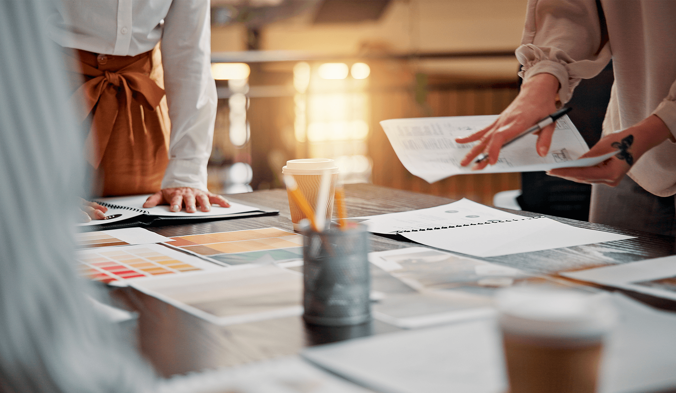Creative professionals reviewing branding materials and color swatches on table during marketing strategy session with coffee and design mockups.