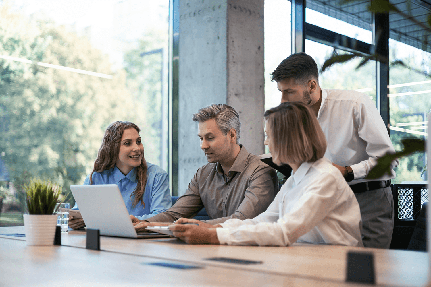 A team of four marketing professionals collaborating around a laptop in a modern office, reviewing data together as part of a backlink analysis or SEO strategy session.