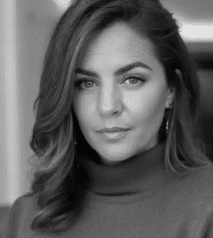 Kelsey Libert portrait wearing a turtleneck, with styled brown hair and a softly blurred indoor background.