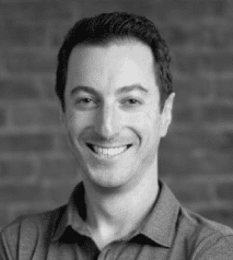 Michael Baynes smiling, wearing a polo shirt, standing in front of a brick wall background.