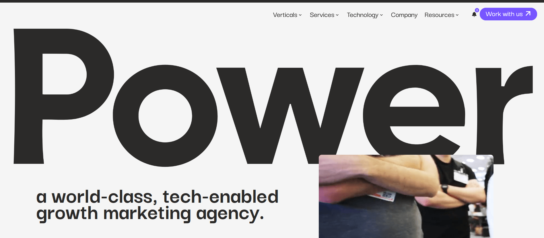 Large black text reading “Power” dominates the center of a website landing page, with the tagline below stating, “a world-class, tech-enabled growth marketing agency.” A smaller image overlay in the lower right corner shows two people with crossed arms wearing conference badges and dark clothing.